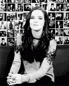 a woman is sitting on a couch in front of a wall of pictures .