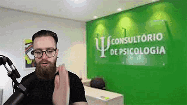 a man with a beard and glasses is standing in front of a microphone in front of a sign that says consultorio
