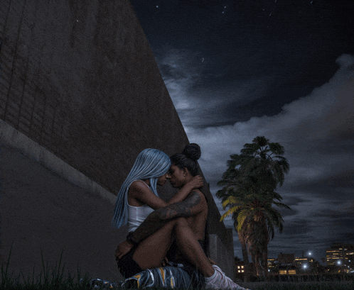 a couple sitting next to each other in front of a brick wall at night