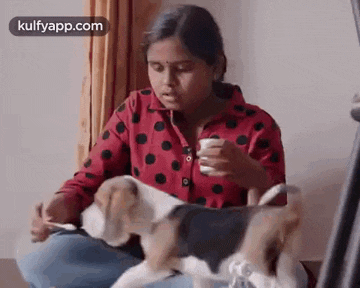 a girl is sitting on the floor with a beagle dog and a cup of coffee .