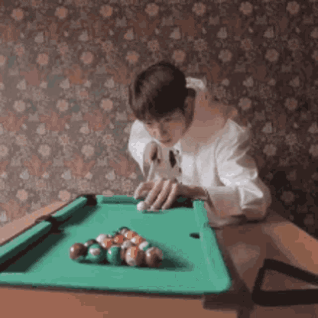 a man is playing pool on a table with a floral wallpaper behind him .