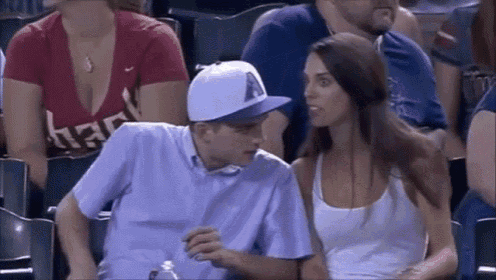 a man and a woman are sitting in the stands at a baseball game and the woman is looking at the man .