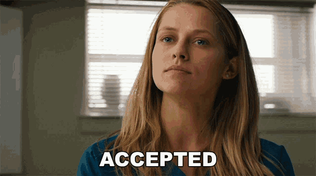 a woman in a blue shirt says accepted in front of a window