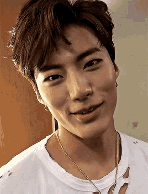 a close up of a young man wearing a white shirt and a gold necklace