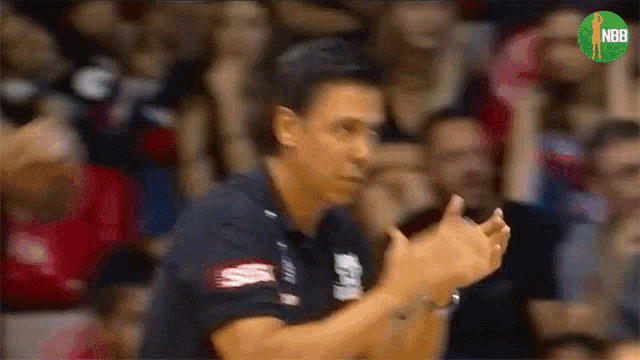 a man applauds in front of a crowd with the nba logo on the bottom right