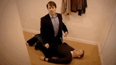 a man in a suit is kneeling next to another man laying on the floor .
