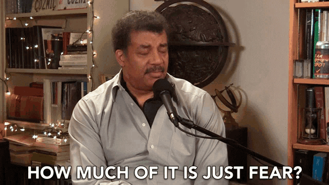 a man sitting in front of a microphone with the words " how much of it is just fear " above him