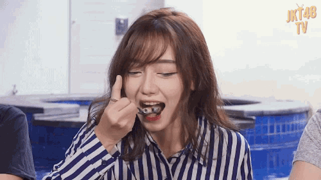 a girl in a striped shirt is eating something with the word jkt48 on the bottom right
