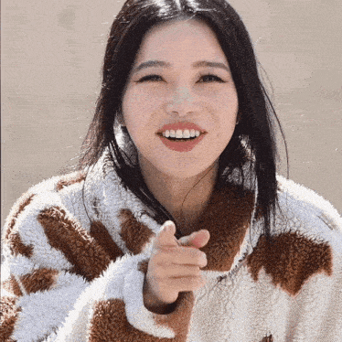 a woman wearing a brown and white sweater is smiling and pointing