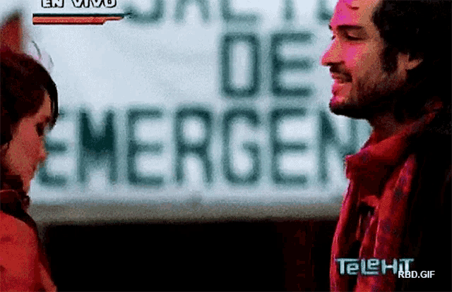 a man and a woman are looking at each other in front of a sign that says emergen