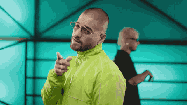 a man wearing glasses and a neon green jacket points at the camera