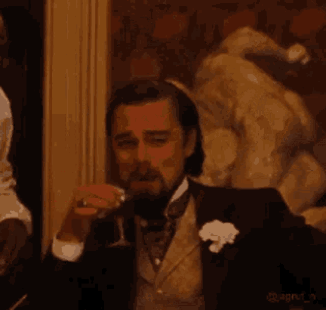 a man in a suit and tie is smoking a cigarette and drinking a glass of wine .