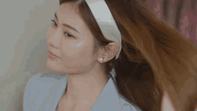 a woman wearing a white headband and earrings looks at her hair