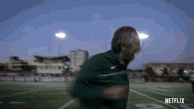 a man in a green nike jacket is running on a football field with netflix written on the bottom