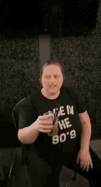 a woman wearing a black t-shirt that says `` made in the 90 's '' is holding a glass of beer .