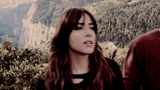 a woman is standing in front of a mountain with a man standing behind her .