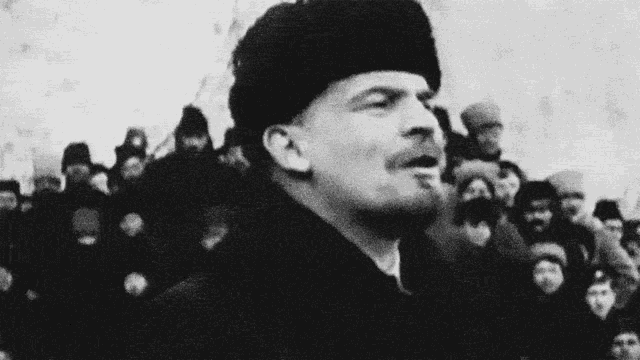 a black and white photo of a man in a hat speaking to a crowd .