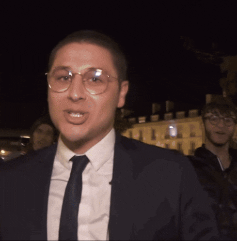 a man wearing glasses and a suit and tie looks at the camera