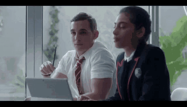 a man and a woman are sitting next to each other in front of a laptop .