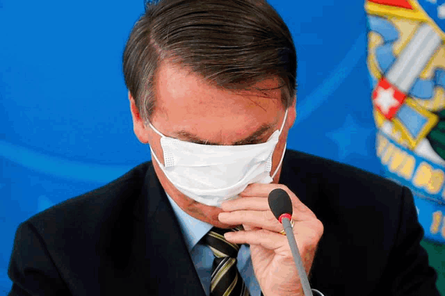 a man wearing a mask is speaking into a microphone in front of a flag that says virado