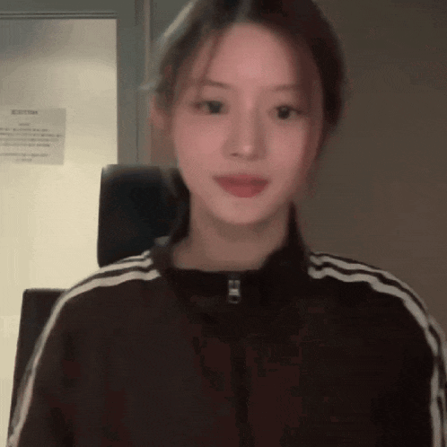 a woman wearing a brown jacket with white stripes on the sleeves looks at the camera