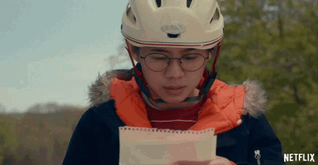 a person wearing a helmet and glasses is looking at a piece of paper that says netflix on the bottom