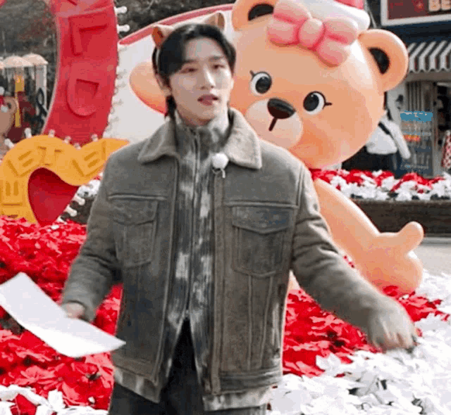 a man in a jacket is standing in front of a giant teddy bear statue .