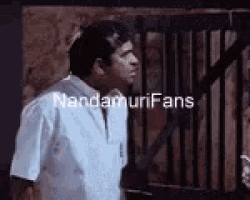 a man in a white shirt is standing in front of a fence with the words nandamurifans on it