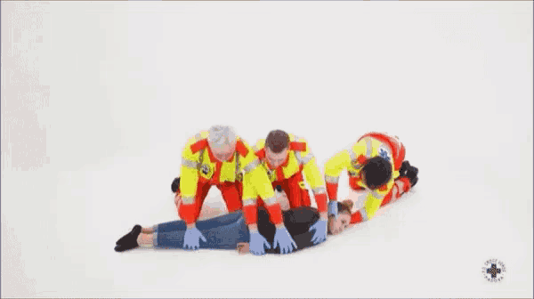 a group of paramedics are helping a woman laying on the floor .