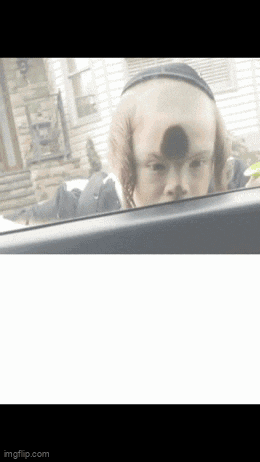 a child with a shaved head is looking out a car window .