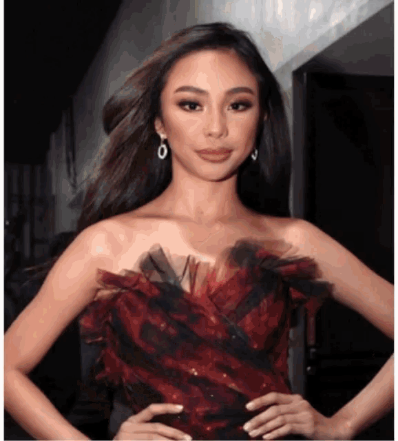 a woman wearing a red and black dress and earrings stands with her hands on her hips