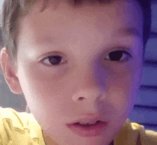 a close up of a young boy 's face in a yellow shirt .
