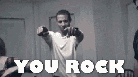 a man in a white shirt is pointing at the camera with the words `` you rock '' above him .