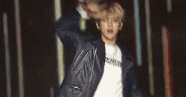 a man in a leather jacket is dancing on a stage in front of a colorful background .