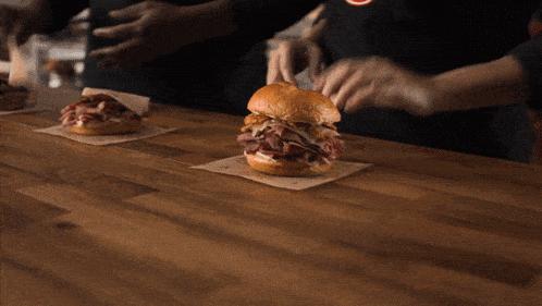a person wearing gloves is holding a beef sandwich on a table