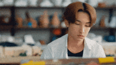 a young man in a white shirt is sitting at a table with his eyes closed in a room .