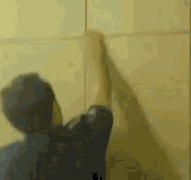 a man is standing in front of a yellow wall holding a piece of paper .