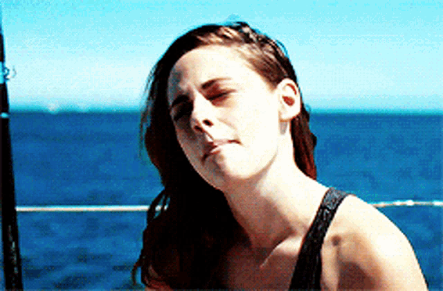 a woman in a black tank top is standing in front of a body of water