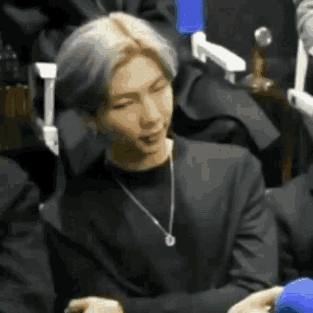 a man in a black suit and a necklace is sitting in a chair .
