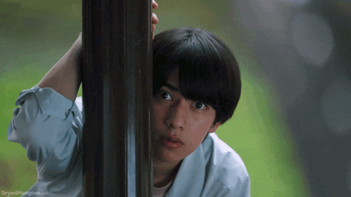 a young man peeking out from behind a pole with the website dryedmangoes.com in the bottom right corner