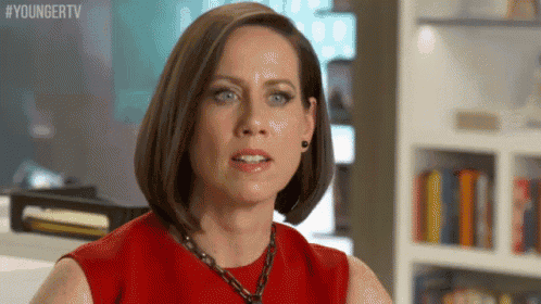 a woman in a red dress is making a funny face while sitting in front of a bookshelf .