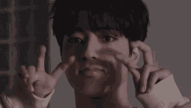 a young man is making a peace sign with his hands while looking at the camera .