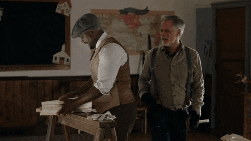 two men are standing next to each other in a room with a map on the wall