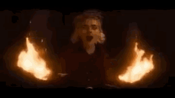 a man is standing in front of a wall of flames in a dark room .