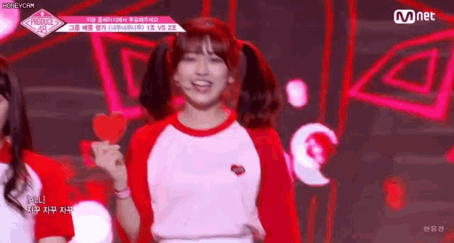a girl in a red and white shirt is holding a red heart on a stick .