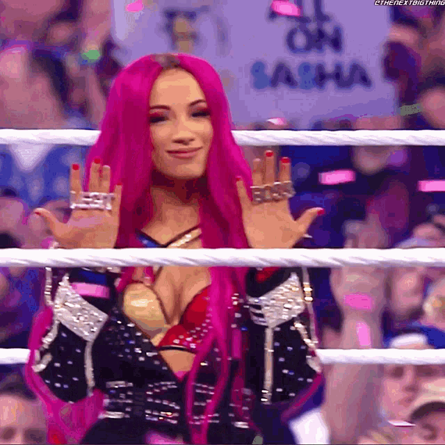 a woman with pink hair is standing in a wrestling ring with her hands in the air .