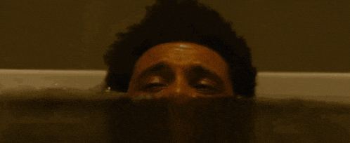 a man is laying in a bathtub with his eyes closed and his head sticking out of the water .