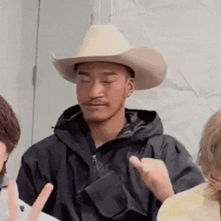 a man wearing a cowboy hat and a black jacket is giving the peace sign .