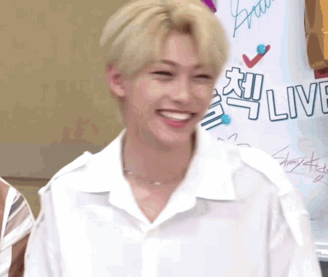 a young man with blonde hair is smiling in front of a sign that says live