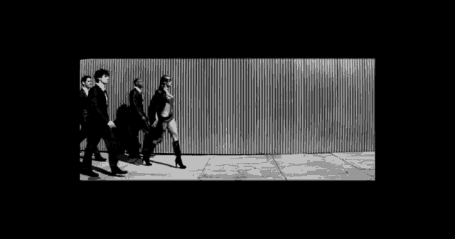 a black and white photo of a group of men and a woman walking down a street